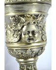 Silver plate urn with figural cherubs and decorative leaf patterns, close-up of bowl details.