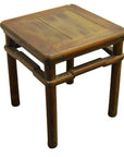 Close-up of a small, square natural-stain elm wood table or stool with four round legs.