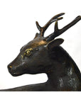 Bronze sitting deer sculpture with detailed antlers and textured surface, close-up view.