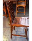 Brown wooden Arts & Crafts style chair with tall backrest and flat seat on indoor wooden floor.