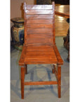 Brown wood Arts & Crafts style chair with slatted back and seat, indoors next to table and ceramic decor item.
