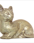Brass cat figurine with engraved fur and alert ears, seated, close-up against plain background.