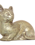 Brass cat figurine with engraved fur and alert ears, seated, close-up against plain background.