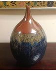 Close-up of a glossy ceramic vase with a narrow neck, featuring gradient brown-blue hues on a wooden surface.