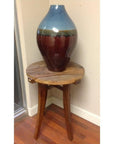 Blue and brown ceramic vase on a small round mango wood table in a corner with wood flooring.