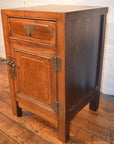 Wooden side cabinet with butterfly brass hardware, latch, drawer, and door on a wooden floor.