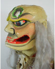 Vibrant wooden mask with exaggerated features and long gray hair in traditional colors, close-up on white background.