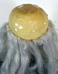 Yellowed plastic dome with cracks and long gray hair strands, vintage opera doll style, close-up.