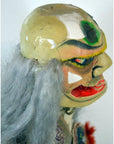 Painted ceramic mask with gray hair, bold features, and a green spot on forehead, close-up.