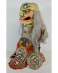 Gray-haired fabric puppet with fierce face and embroidered clothing, close-up, indoor setting.