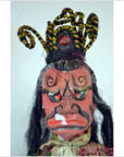 Close-up of a Taiwan Opera Doll with a red face, elaborate headpiece, and long black hair against a plain background.