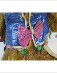 Close-up of doll with blue sequin vest, pink bow tie, and green decorations.