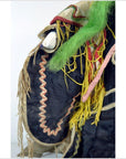 Close-up of Taiwan Opera Doll with green hair, yellow-tan fringe, and zigzag trim on vibrant dark fabric.