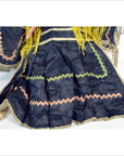 Close-up of colorful fabric Taiwan Opera Doll skirt with zigzag trim, yellow fringe, and playful decorative details.