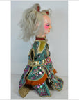 Side view of a Taiwan Opera Doll with white hair, painted face, and bold-patterned sequin costume.