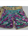 Pink and green fabric Taiwan opera doll with sequined shorts, gold trim, and decorative waistband, indoor setting.