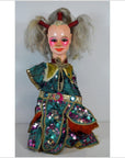 Close-up of Taiwan Opera Doll with painted face, gray hair, sequined gold and red costume, on plain background.