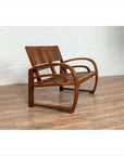 Brown teak wood settee with folding back, looping arms, and cane seat on wooden floor, white brick wall background.