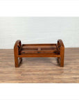 Brown wooden coffee table frame without top beside teak wood settee on wooden floor against white brick wall indoors.