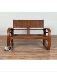 Brown teak wood settee with folding back, looping arms, and cane seat on wooden floor with color chart in front.