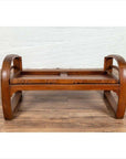 Brown wood coffee table base with curved legs next to a teak wood settee with cane seat and looping arms, indoors.