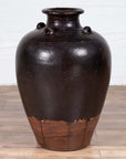 Brown ceramic Thai water jar with four handles, early 20th century, on wooden floor against a light-colored wall.
