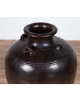 Dark brown glossy ceramic water jar with handles, early 20th c. Thai brownware, on a wooden floor.