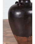 Close-up of brown ceramic Thai water jar with carrying handles, early 20th century, on wooden floor.