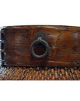 Close-up of brown wood and metal Thai grain basket with rim and metal ring handle, side view.
