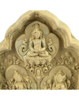 Close-up of an ornate stone terracotta relief featuring a seated figure in meditation, Thai shrine style.