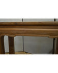 Close-up of brown teak wood table with carved edges and horse hoof feet against a plain background.