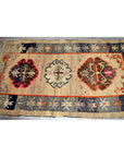 Beige, black, red, and gray wool Tibetan praying rug with geometric and floral patterns on a wooden floor.