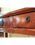 Close-up of antique elmwood triple drawer desk with bronze hardware in a bright, well-lit room.