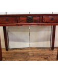 Brown wooden triple drawer desk with bronze hardware and four straight legs, shown on a wooden floor.