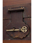 Close-up of a brass key in the lock of an old, dark natural wood trunk.