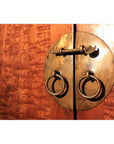 Close-up of round brass lock with rings and latch on warm, textured burl wood cabinet door.