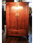 Brown burl wood cabinet with double doors, brass handle, and bottom drawer on a wooden floor.