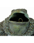 Close-up of weathered verde gris bronze frog statue holding a metal roll.