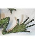 Close-up of greenish bronze frog sculpture with bent leg and webbed foot, light background.