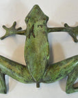 Verde gris bronze frog figurine outstretched on a light background.