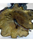 Close-up of green and gold bronze frog sculpture with textured finish and metal stem, lost wax technique.