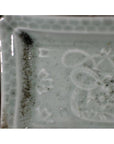 Close-up of a white porcelain dish with hand painted geometric border, black specks, and subtle patterns.