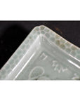 Close-up of light green porcelain dish with engraved rim and hand painted Asian honeycomb pattern.