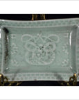 Light blue-green porcelain dish with hand painted geometric border and abstract floral motifs, close-up view.