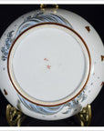 Close-up of base of vintage Asian porcelain plate with blue wave pattern, brown fish, and red Chinese characters at center.