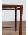 Close-up of brown bamboo table legs with patina on wood floor against a white wall.