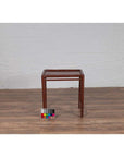 Brown bamboo side table with vintage patina, placed on wooden floor against white brick wall and color chart.