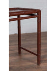 Close-up of brown bamboo table leg with aged patina, on wood floor next to white brick wall.