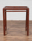 Brown bamboo side table with recessed top and vintage patina, placed on wooden floor next to white brick wall indoors.