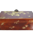 Black lacquered wooden dowry box with gold floral designs and a decorative handle on the lid, shown indoors.